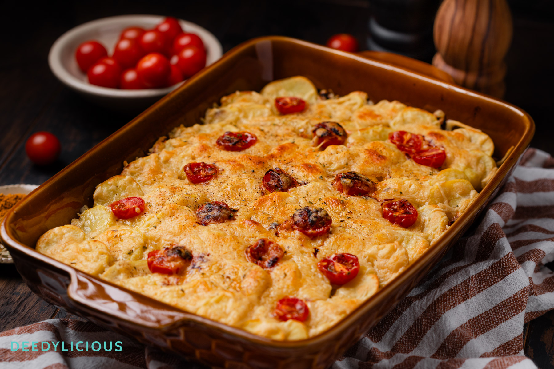 Oranje bruine ovenschaal met daarin de ovenschotel met spitskool, prei en komijn gemaakt door deedylicious. Daar omheen wat tomaatjes en specerijen die in het recept zijn gebruikt.