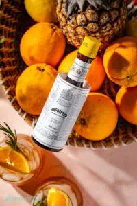 Fles Angostura bitters op een fruitschaal gevuld met sinaasappels, citroenen en een ananas.