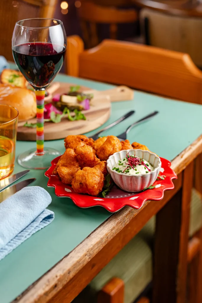 Eettafel met mintgroen topblad in het vegan restaurant Ministerie van Geluk in Zoetermeer, met daarop een rood bordje gevuld met bloemeling en een bakje remouladesaus. Ernaast een glas rode wijn en in de achtergrond zie je nog een borrelplankje met de faux gras. Horeca fotografie door Wendy Pronk van DeedyLicious voor horecazaak in Zoetermeer.